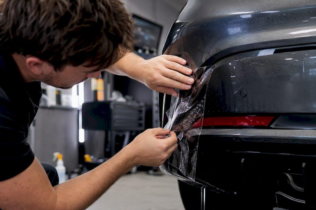 Hands applying clear paint protection film to car panel