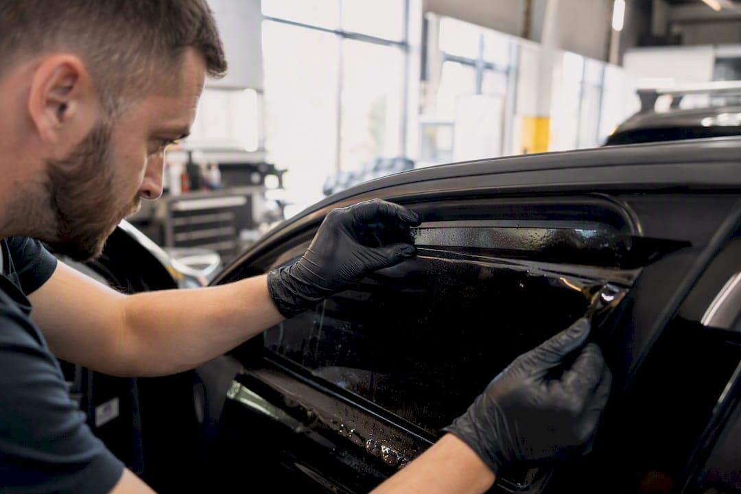Hands applying window tint film on car window edge